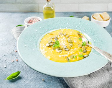 Balkabağı parmesan çorbası kabak çekirdeği, fesleğen yaprakları ve parmesan peyniri wit, mavi arka plan kopya alanı yukarıdan ışık