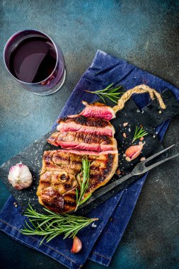 Et ve şarap ahşap kesme tahtası üzerinde çatal ile ızgara biftek dilimlenmiş. Koyu mavi arka plan. Üstten görünüm kopya alanı