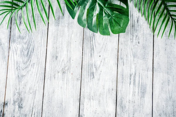 Tropical background. Palm and monstera leaves on wooden grey background. Flatlay, top view, minimal layout, summer concept