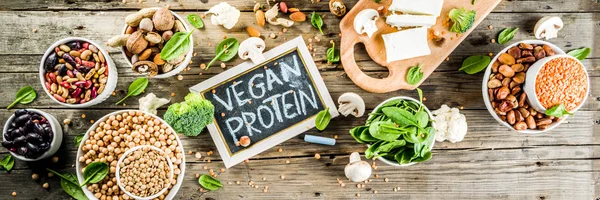 Healthy plant vegan food, veggie protein sources: Tofu, vegan milk, beans, lentils, nuts, soy milk, spinach and seeds. Old wooden background copy space banner