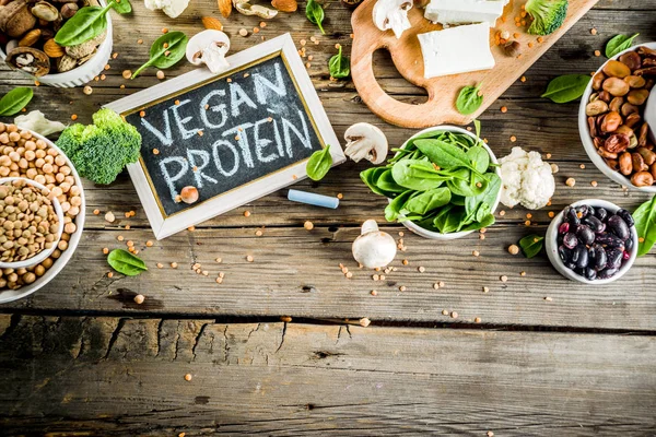 Healthy plant vegan food, veggie protein sources: Tofu, vegan milk, beans, lentils, nuts, soy milk, spinach and seeds. Old wooden background copy space