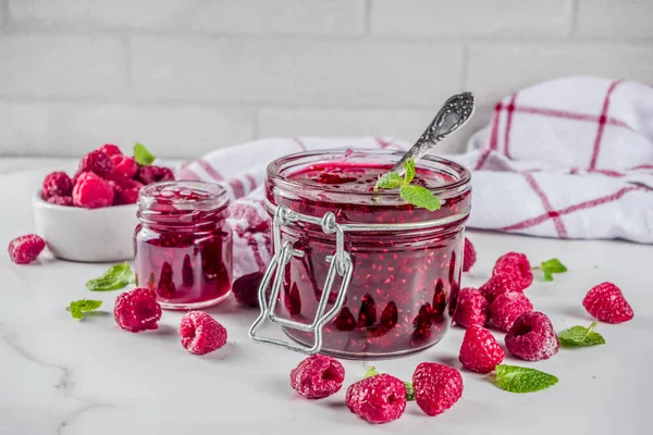 Homemade raspberry jam in two jars with raspberries and mint