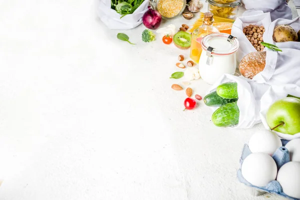 Zero waste shopping and sustanable lifestyle concept, various farm organic vegetables, grains, pasta, eggs and fruits in reusable packaging supermarket bags. copy space top view, white concrete table