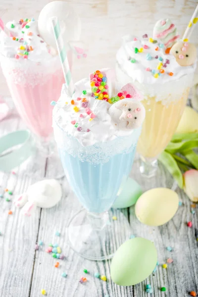 Funny easter food, ideas recipes for children Easter party, colorful blue yellow pink milkshakes with sugar sprinkles, wooden background with Easter egg and bunny rabbit decoration, copy space