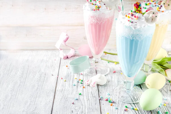 Funny easter food, ideas recipes for children Easter party, colorful blue yellow pink milkshakes with sugar sprinkles, wooden background with Easter egg and bunny rabbit decoration, copy space