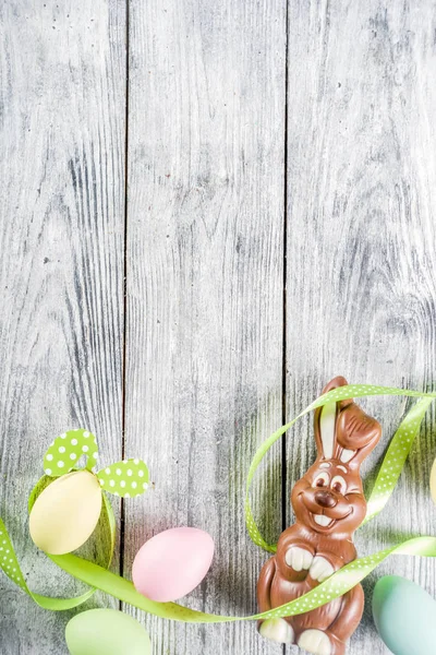 Easter greeting card background with bunny rabbits and colorful eggs, holiday ribbon and tulip flowers, wooden background top view copy space