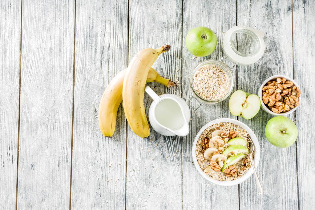 Healthy breakfast oatmeal with nuts ad fruits - apple, banana, walnuts, With milk on wooden background copy space