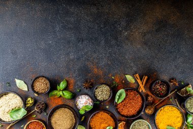 Pişirmek için baharat ve ot seti. Renkli baharatlı küçük kaseler fesleğen, biber, safran, tuz, paprika, zerdeçal. Siyah taş tablo üzerinde üst görünüm kopyalama alanı