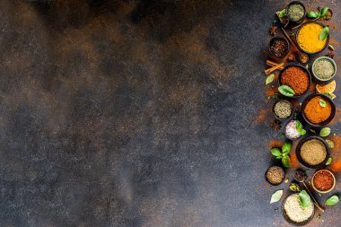 Pişirmek için baharat ve ot seti. Renkli baharatlı küçük kaseler fesleğen, biber, safran, tuz, paprika, zerdeçal. Siyah taş tablo üzerinde üst görünüm kopyalama alanı
