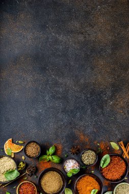 Pişirmek için baharat ve ot seti. Renkli baharatlı küçük kaseler fesleğen, biber, safran, tuz, paprika, zerdeçal. Siyah taş tablo üzerinde üst görünüm kopyalama alanı