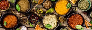 Pişirmek için baharat ve ot seti. Renkli baharatlı küçük kaseler fesleğen, biber, safran, tuz, paprika, zerdeçal. Kırsal ahşap masa arka planında, üst görünüm kopyalama alanı