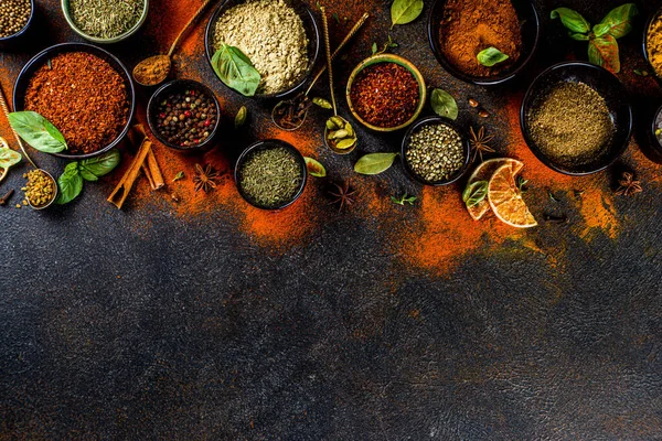 Set of Spices and herbs for cooking. Small bowls with colorful  seasonings and spices - basil, pepper, saffron, salt, paprika, turmeric. On black stone table top view copy space