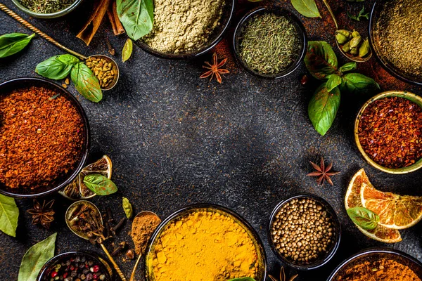 Set of Spices and herbs for cooking. Small bowls with colorful  seasonings and spices - basil, pepper, saffron, salt, paprika, turmeric. On black stone table top view copy space
