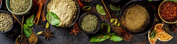 Set of Spices and herbs for cooking. Small bowls with colorful  seasonings and spices - basil, pepper, saffron, salt, paprika, turmeric. On black stone table top view copy space