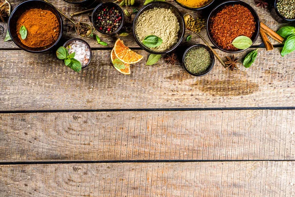 Set of Spices and herbs for cooking. Small bowls with colorful  seasonings and spices - basil, pepper, saffron, salt, paprika, turmeric. On rustic wooden plank table background, top view copy space