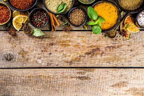 Set of Spices and herbs for cooking. Small bowls with colorful  seasonings and spices - basil, pepper, saffron, salt, paprika, turmeric. On rustic wooden plank table background, top view copy space