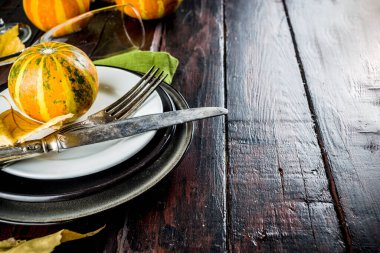 Sonbahar ve Şükran Günü kutlaması masaları. Tabaklar, çatal bıçaklar, cam ve küçük balkabaklarıyla düz yatak. Tatil dekorasyonu, ahşap arka plan, üst manzara, kopyalama alanı.