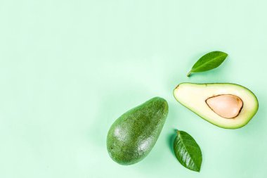 Çiğ organik avokado, açık yeşil zemin üzerinde dilimlenmiş avokado, yeşil yapraklı, basit desen düzeni, üst görünüm kopyalama alanı
