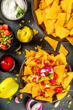 Eritilmiş peynirli cips ve çeşitli geleneksel Meksika sosları, salsa ve jalapeno, koyu gri arka plan fotokopi alanı