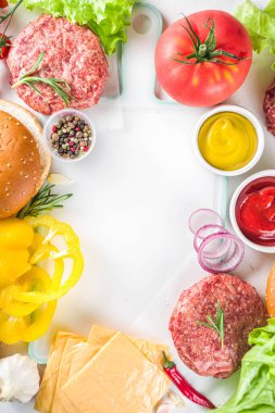 Hamburger arka planı. Çeşitli cheeseburger ve sığır burger malzemelerini hazırla - çörek, domates, soğan, marul, sos, peynir ve çiğ burger pirzolası, ızgara için hazır. Burger bbq parti festivali konsepti, üst görünüm kopyalama alanı