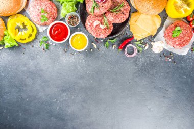 Hamburger arka planı. Çeşitli cheeseburger ve sığır burger malzemelerini hazırla - çörek, domates, soğan, marul, sos, peynir ve çiğ burger pirzolası, ızgara için hazır. Burger bbq parti festivali konsepti, üst görünüm kopyalama alanı