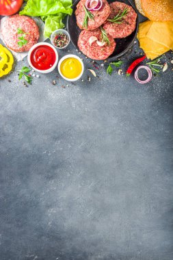 Hamburger arka planı. Çeşitli cheeseburger ve sığır burger malzemelerini hazırla - çörek, domates, soğan, marul, sos, peynir ve çiğ burger pirzolası, ızgara için hazır. Burger bbq parti festivali konsepti, üst görünüm kopyalama alanı