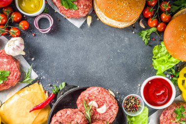 Hamburger arka planı. Çeşitli cheeseburger ve sığır burger malzemelerini hazırla - çörek, domates, soğan, marul, sos, peynir ve çiğ burger pirzolası, ızgara için hazır. Burger bbq parti festivali konsepti, üst görünüm kopyalama alanı