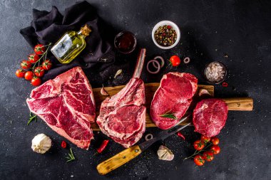 Bir dizi klasik, alternatif çiğ et, dana bifteği - şato mignon, t-bone, tomahawk, striploin, fileto, New York bifteği. Siyah taş kesme masasının üstünde düz bir görünüm vardı.