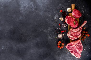 Bir dizi klasik, alternatif çiğ et, dana bifteği - şato mignon, t-bone, tomahawk, striploin, fileto, New York bifteği. Siyah taş kesme masasının üstünde düz bir görünüm vardı.