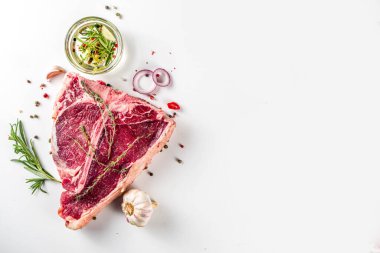 Et arka planı yapıyorum. Çiğ biftekli biftek, arka planda beyaz masa manzarasında yemek pişirmek için baharatlar ve otlar.