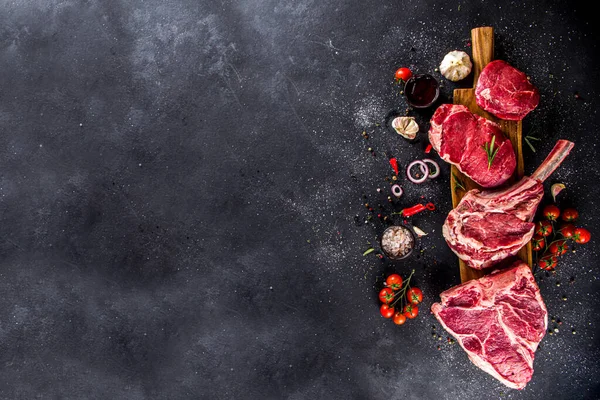 Set of various classic, alternative raw meat, veal beef steaks - chateau mignon, t-bone, tomahawk, striploin, tenderloin, new york steak. Flat lay top view on black stone cutting table