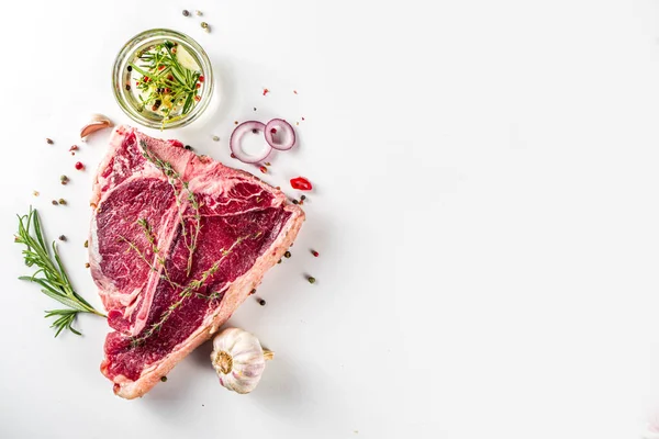 Cooking meat background. Raw aged beef t-bone steak, with spices and herbs for cooking on white table background top view
