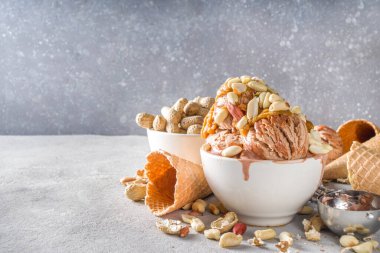 Fıstık ezmeli dondurma. Fıstık ezmeli tatlı fıstık dondurması ve kremalı waffle külahlı gri taş arka planda bir sürü fıstık.