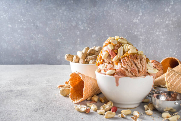 Peanut butter ice cream. Sweet peanut ice cream with peanut butter topping and a lot of peanuts, on grey stone background with icecream waffle cones