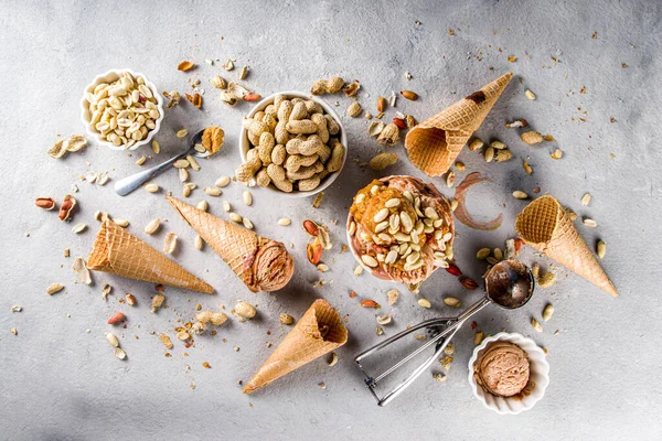 Peanut butter ice cream. Sweet peanut ice cream with peanut butter topping and a lot of peanuts, on grey stone background with icecream waffle cones