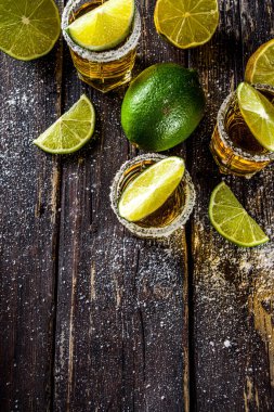 Altın tekila shot 'ları. Üç tekila bardağı tuz ve limon dilimli, ahşap arka planda fotokopi alanı