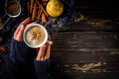 Sonbahar tatlısı, Chai Buttered Rum, Balkabağı Turtası veya Baharatlı Kahve Latte. Sıcak sonbahar arka planı. Geleneksel latte fincanını elinde tut, kırsal ahşap arka planda.