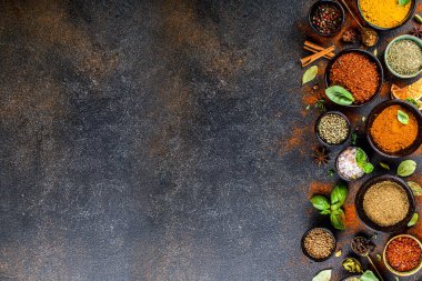 Pişirmek için baharat ve ot seti. Renkli baharatlı küçük kaseler fesleğen, biber, safran, tuz, paprika, zerdeçal. Siyah taş tablo üzerinde üst görünüm kopyalama alanı
