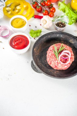 Hamburger arka planı. Çeşitli cheeseburger ve sığır burger malzemelerini hazırla - çörek, domates, soğan, marul, sos, peynir ve çiğ burger pirzolası, ızgara için hazır. Burger bbq parti festivali konsepti, üst görünüm kopyalama alanı