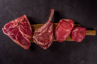Bir dizi klasik, alternatif çiğ et, dana bifteği - şato mignon, t-bone, tomahawk, striploin, fileto, New York bifteği. Siyah taş kesme masasının üstünde düz bir görünüm vardı.