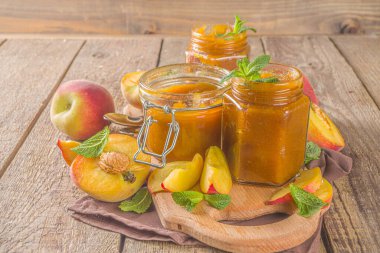 Farklı kavanozlarda ev yapımı şeftali reçeli ve ahşap arka planda taze organik şeftali.
