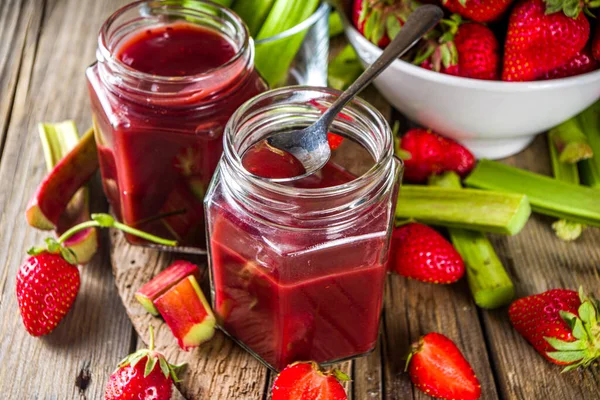 Homemade strawberry rhubarb jam or sauce, with fresh rhubarb and strawberries and spices, wooden rustic background copy space