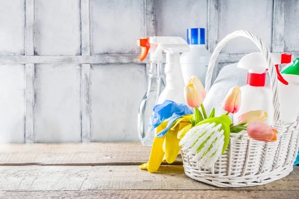 Spring home cleaning and housekeeping concept, Basket with cleaning items, utensils, supplies. Copy space over wooden background with spring blossom flowers