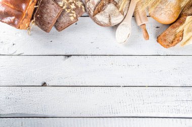 Çeşitli ekmek setleri. Birçok farklı buğday, tahıl ve çavdar ekmeği çavdar ve buğday, un ve fırıncı aletleriyle beyaz ahşap arka planda.
