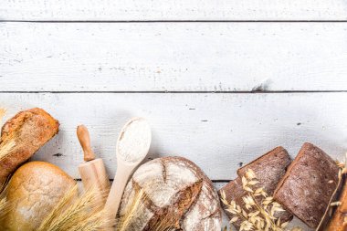Çeşitli ekmek setleri. Birçok farklı buğday, tahıl ve çavdar ekmeği çavdar ve buğday, un ve fırıncı aletleriyle beyaz ahşap arka planda.