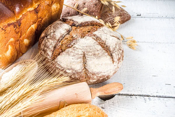 Çeşitli ekmek setleri. Birçok farklı buğday, tahıl ve çavdar ekmeği çavdar ve buğday, un ve fırıncı aletleriyle beyaz ahşap arka planda.