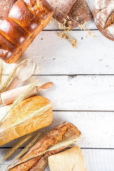 Çeşitli ekmek setleri. Birçok farklı buğday, tahıl ve çavdar ekmeği çavdar ve buğday, un ve fırıncı aletleriyle beyaz ahşap arka planda.