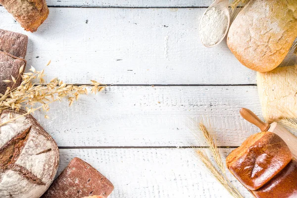 Çeşitli ekmek setleri. Birçok farklı buğday, tahıl ve çavdar ekmeği çavdar ve buğday, un ve fırıncı aletleriyle beyaz ahşap arka planda.