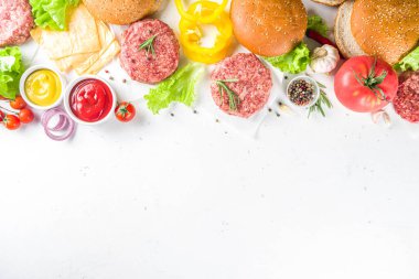 Hamburger arka planı. Çeşitli cheeseburger ve sığır burger malzemelerini hazırla - çörek, domates, soğan, marul, sos, peynir ve çiğ burger pirzolası, ızgara için hazır. Burger bbq parti festivali konsepti, üst görünüm kopyalama alanı