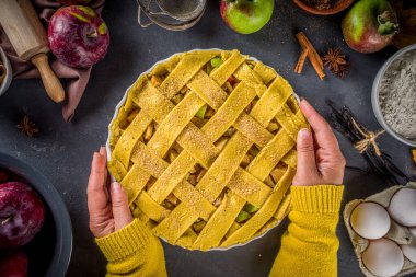 Sonbahar elmalı turta pişirme geçmişi. Çiğ geleneksel elmalı turta, fırın malzemeleri ve çatal bıçaklar, siyah beton arka plan fotokopi alanı, kız eli pastayı tutuyor. 